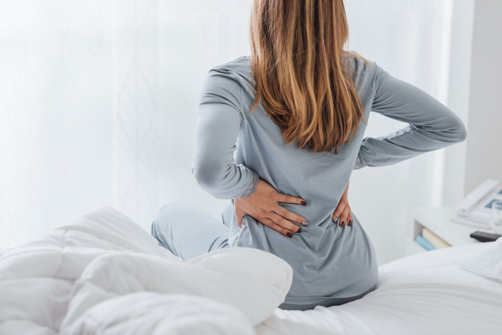 A woman sitting up in bed holding her back in pain in El Paso.