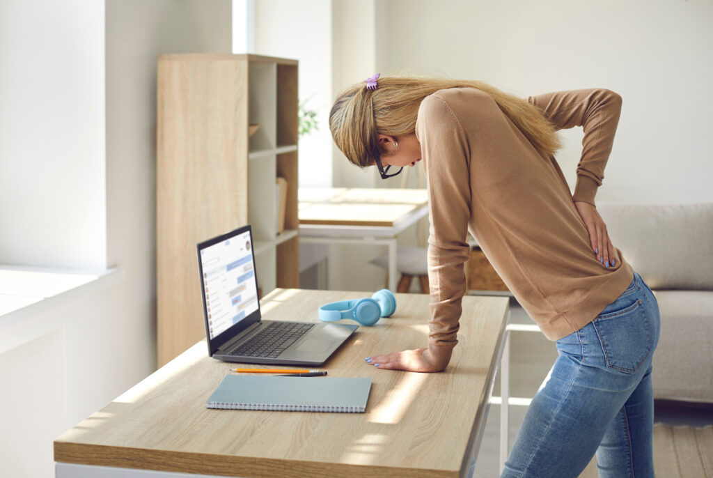 A woman leaning over a desk grabbing her back in pain in El Paso.